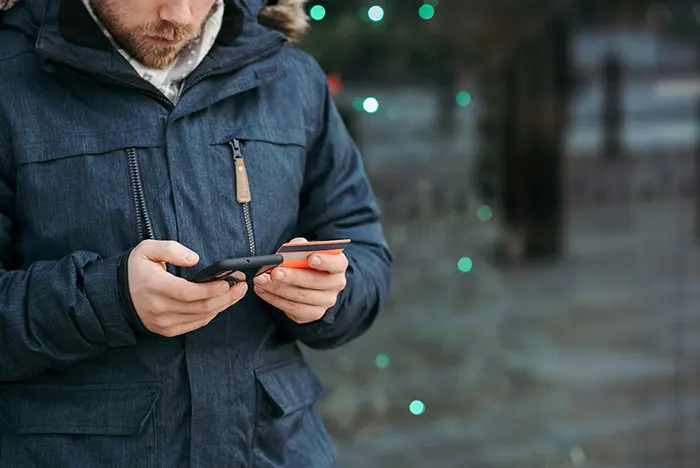 Man browsing his smartphone and holding a credit card on street