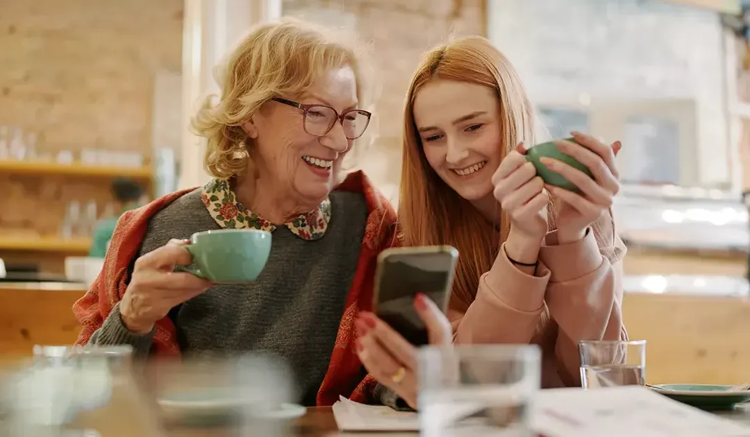 An elderly woman holding a mobile phone with a teenage girl