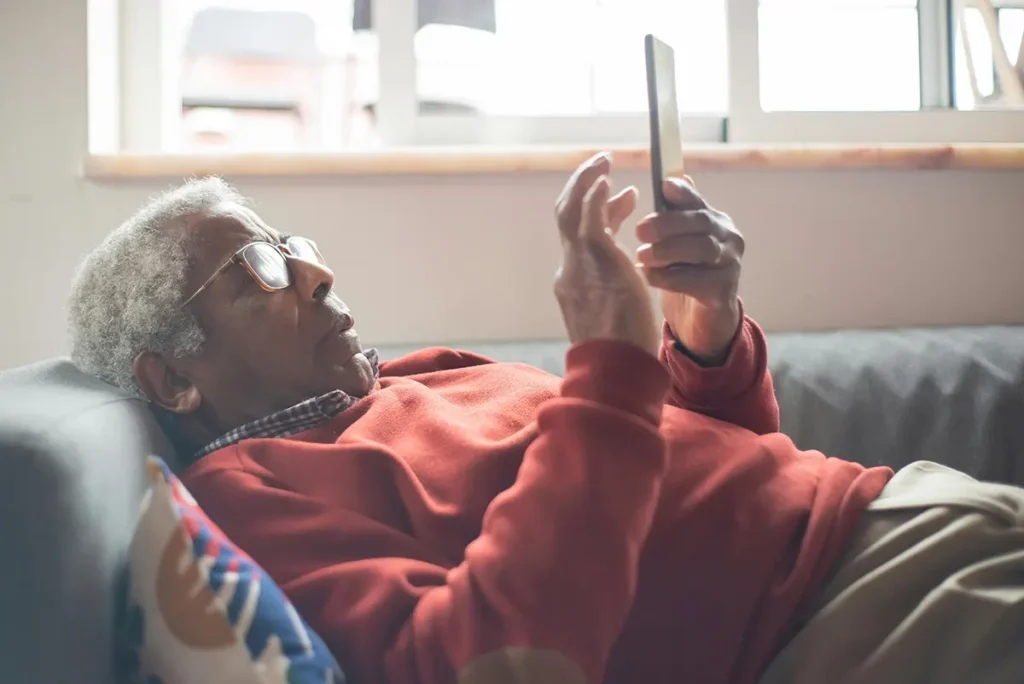 Elderly man sitting on a couch holding a mobile phone